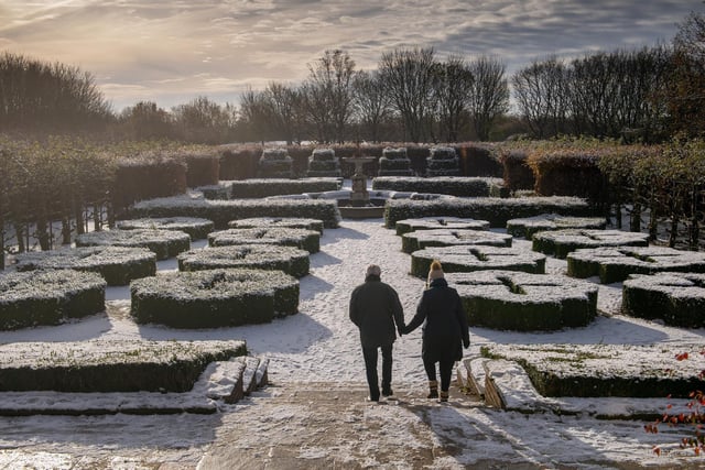 A couple hold hands while walking in the snow at Temple Newsam.