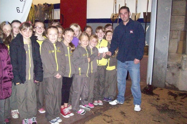 Pittenweem Brownies celebrated their 100th Birthday in 2014 by having a sponsored silence to raise money for charity.  The sponsored silence was so successful that £500 was raised.  The Brownies decided to donate £100 to five charities including Anstruther Lifeboat.  The photograph shows Lacey Greig handing the cheque to William Wood, Coxswain of Anstruther Lifeboat during a tour of the RNLI Lifeboat shed.  The other charities to benefit were Smile Train, Save the Children, Make a Wish Foundation and CHAS.