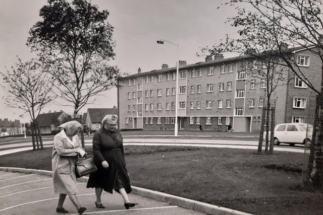 Two women out walking in a Glenrothes street, complete with headscarves - but note the lack of traffic on the road.