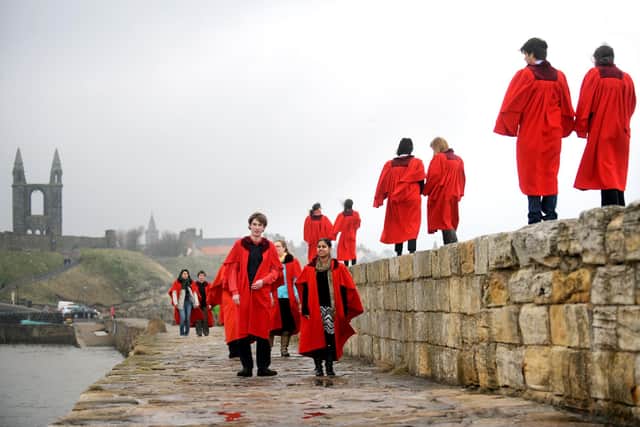 Students from the University of St Andrews walk along the harbour wall wearing their infamous red gowns.(Pic: TSPL)