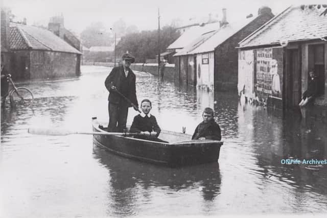 Three boys paddling a boat in Burnside, Cupar, during the floods of July 1916. In the boat are John Bett (standing), Patterson (with the oar) and William Meldrum, sitting in the window is D.Gordon.