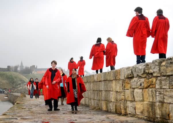 Students from the University of St Andrews walk along the harbour wall wearing their infamous red gowns.